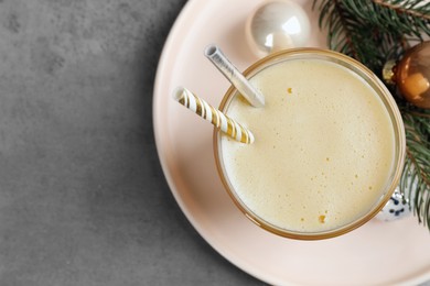 Photo of Glass of delicious eggnog and decorated fir branch on gray table, flat lay. Space for text