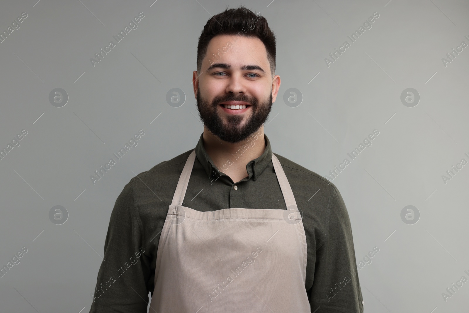 Photo of Smiling man in kitchen apron on grey background. Mockup for design