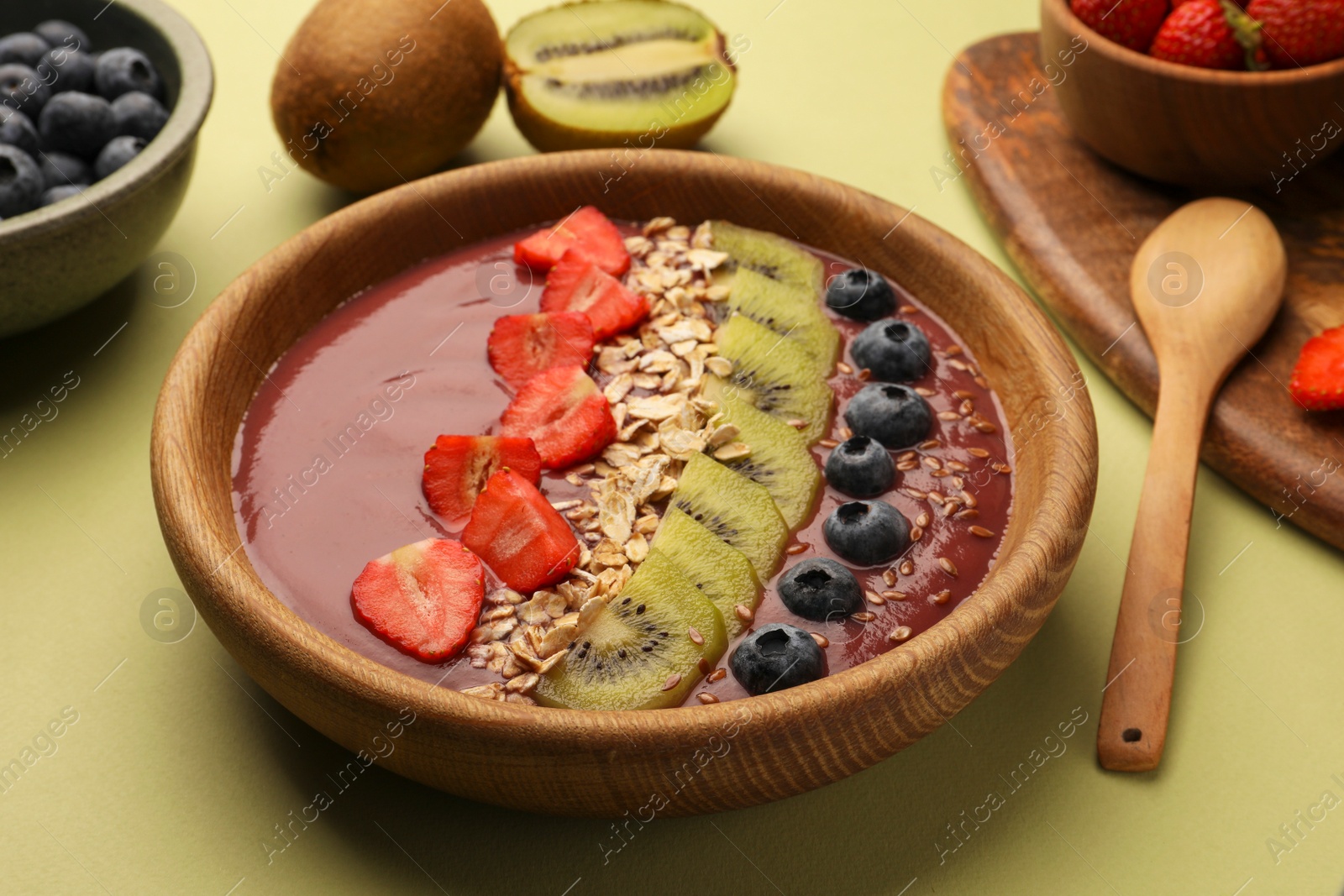 Photo of Bowl of delicious smoothie with fresh blueberries, strawberries, kiwi slices and oatmeal on light green table, closeup