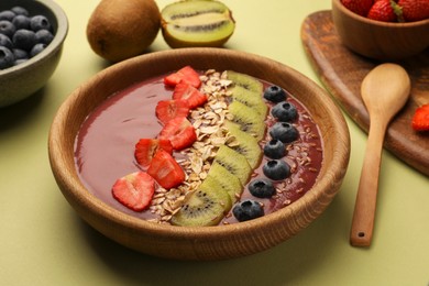 Photo of Bowl of delicious smoothie with fresh blueberries, strawberries, kiwi slices and oatmeal on light green table, closeup