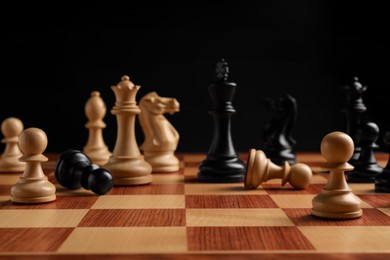 Many chess pieces on wooden checkerboard against black background, selective focus