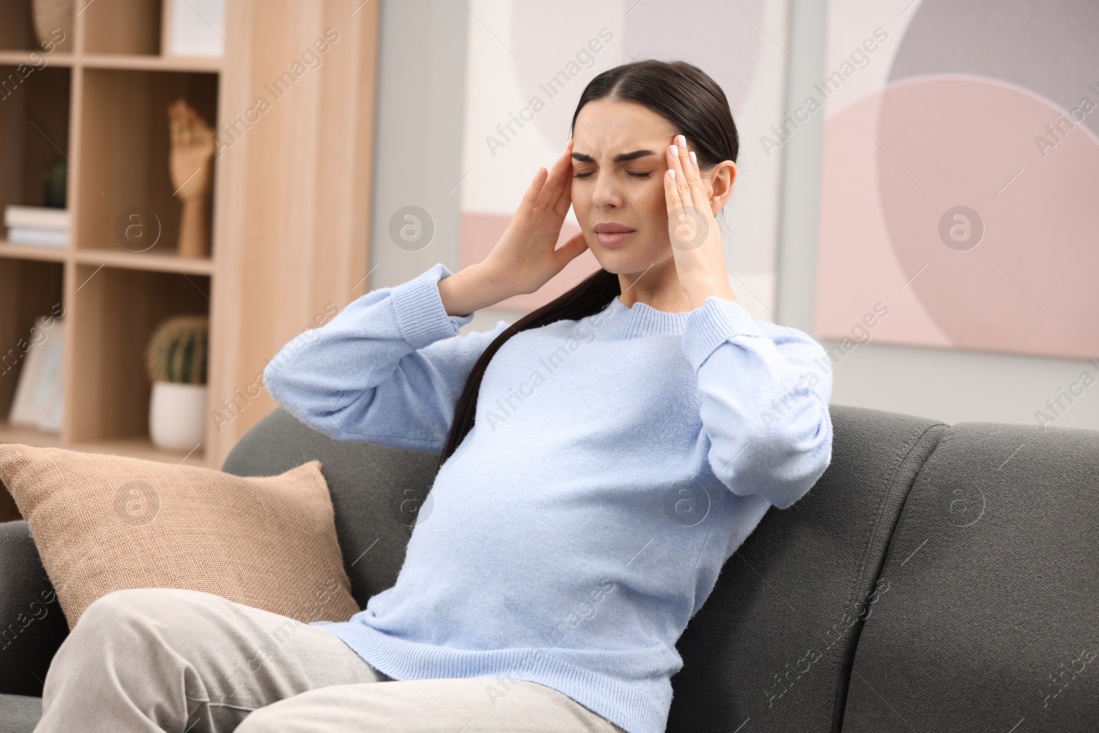 Photo of Pregnant woman suffering from headache on sofa at home