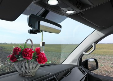 Beautiful flowers and air freshener hanging on rear view mirror in car