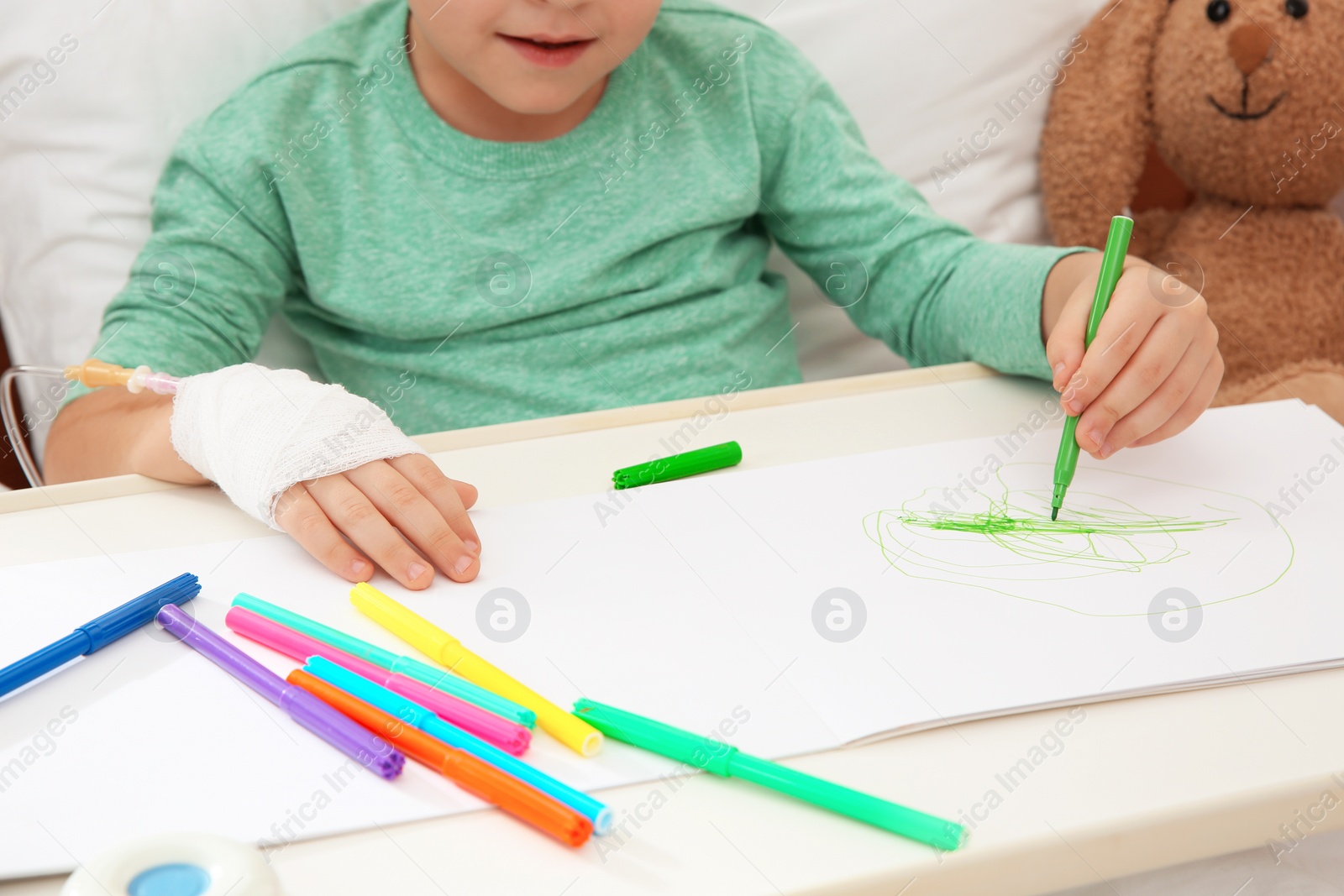 Photo of Little child with infusion drip drawing in hospital bed, closeup