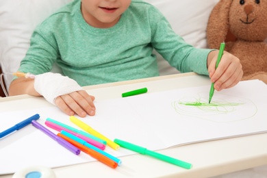 Photo of Little child with infusion drip drawing in hospital bed, closeup