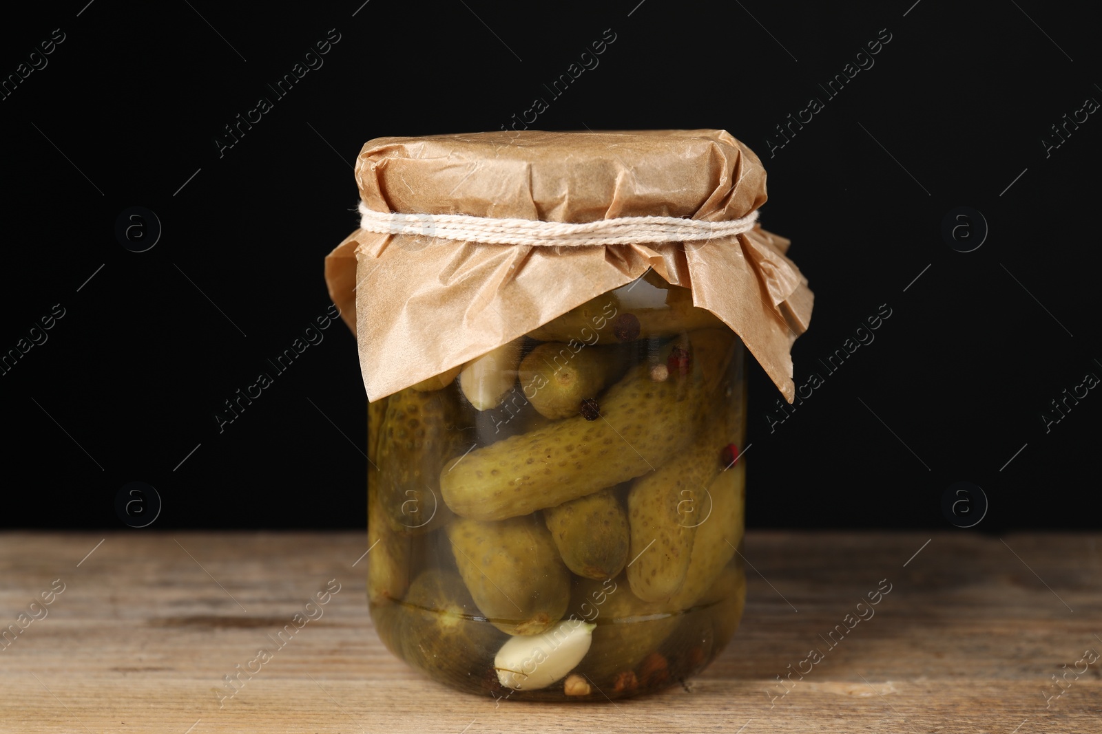 Photo of Tasty pickled cucumbers in glass jar on wooden table against black background