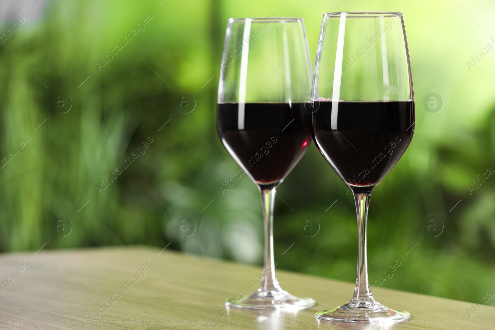 Photo of Tasty red wine in glasses on wooden table, space for text