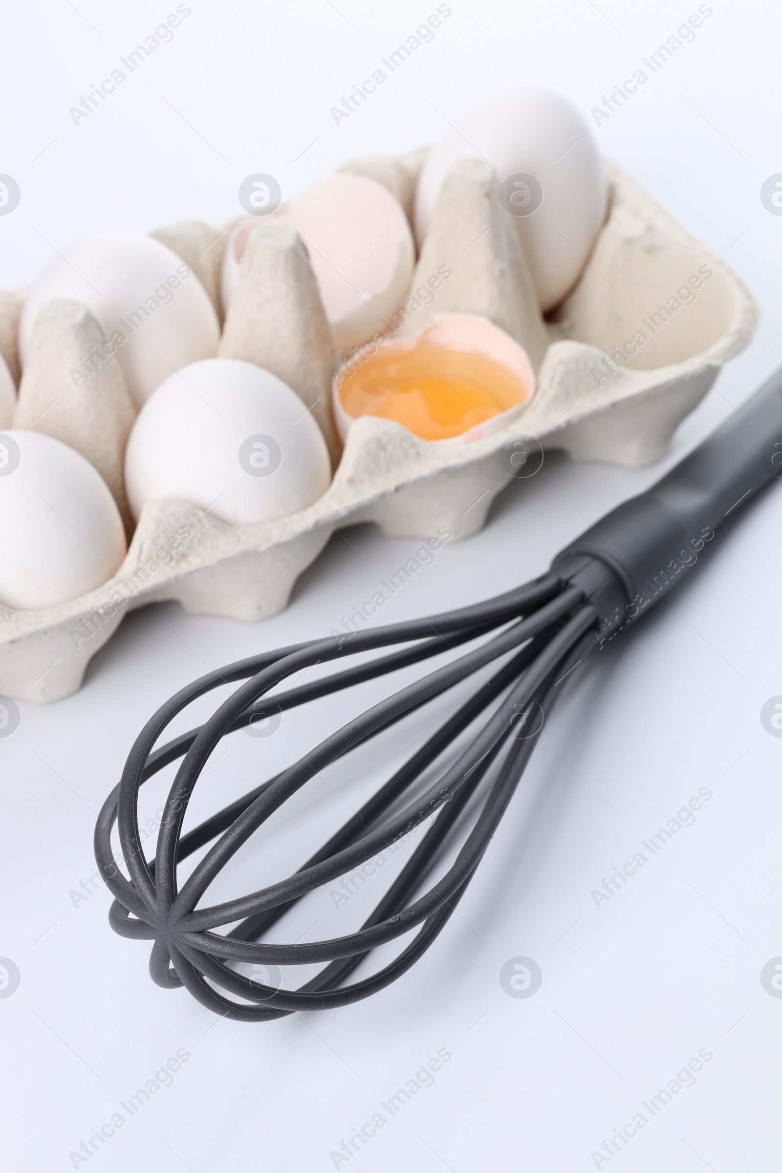 Photo of Whisk and carton with raw eggs isolated on white