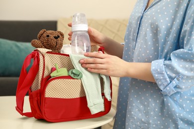 Photo of Woman putting baby`s bottle into mother`s bag at white table indoors, closeup