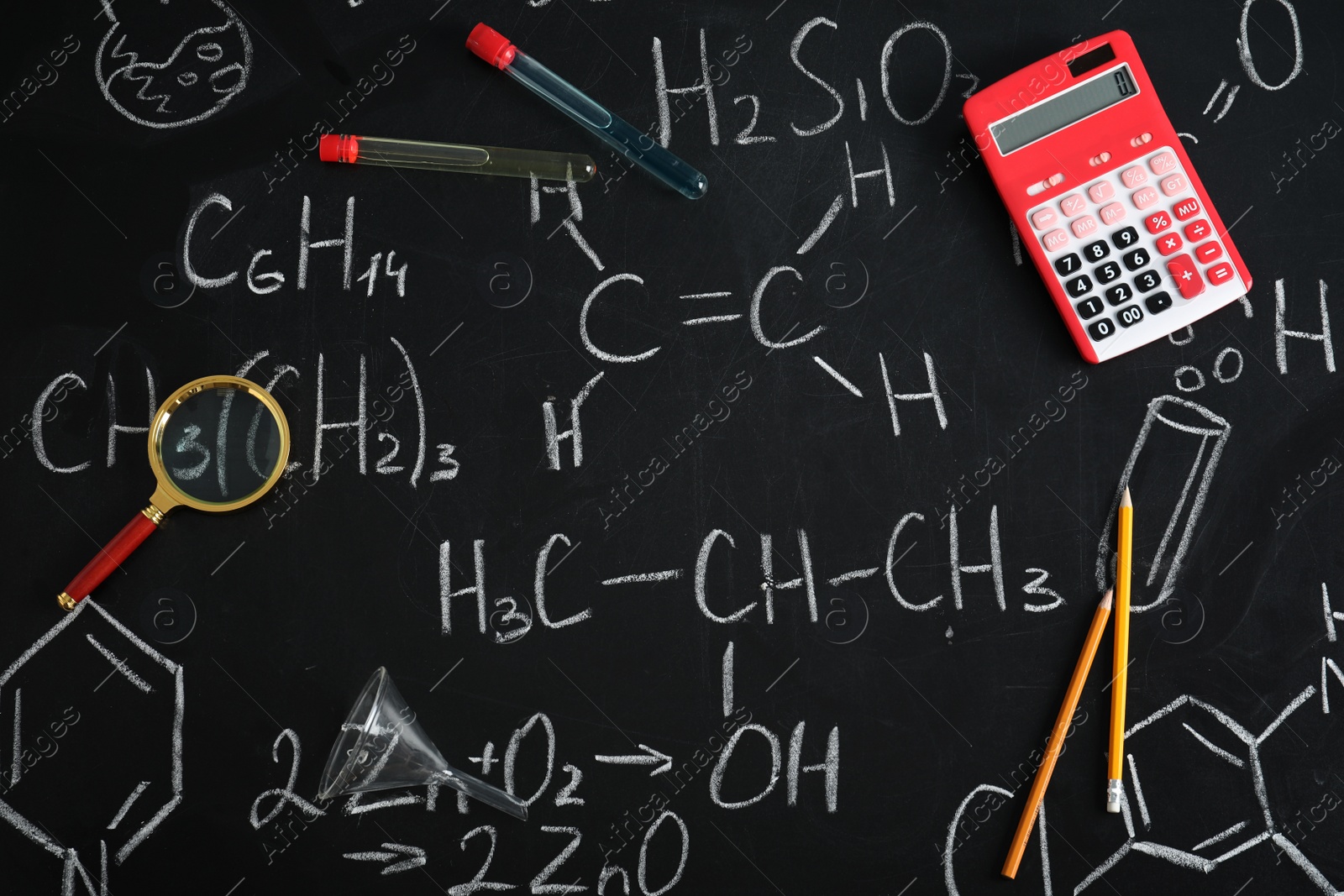 Photo of Laboratory glassware and school supplies on blackboard with chemical formulas, flat lay