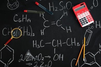 Laboratory glassware and school supplies on blackboard with chemical formulas, flat lay