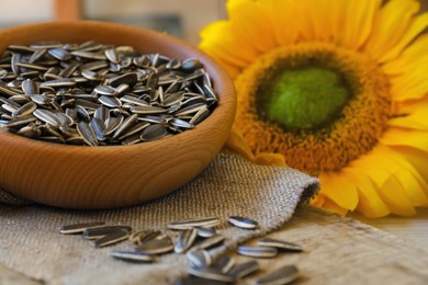 Photo of Organic sunflower seeds and flower on wooden table, closeup