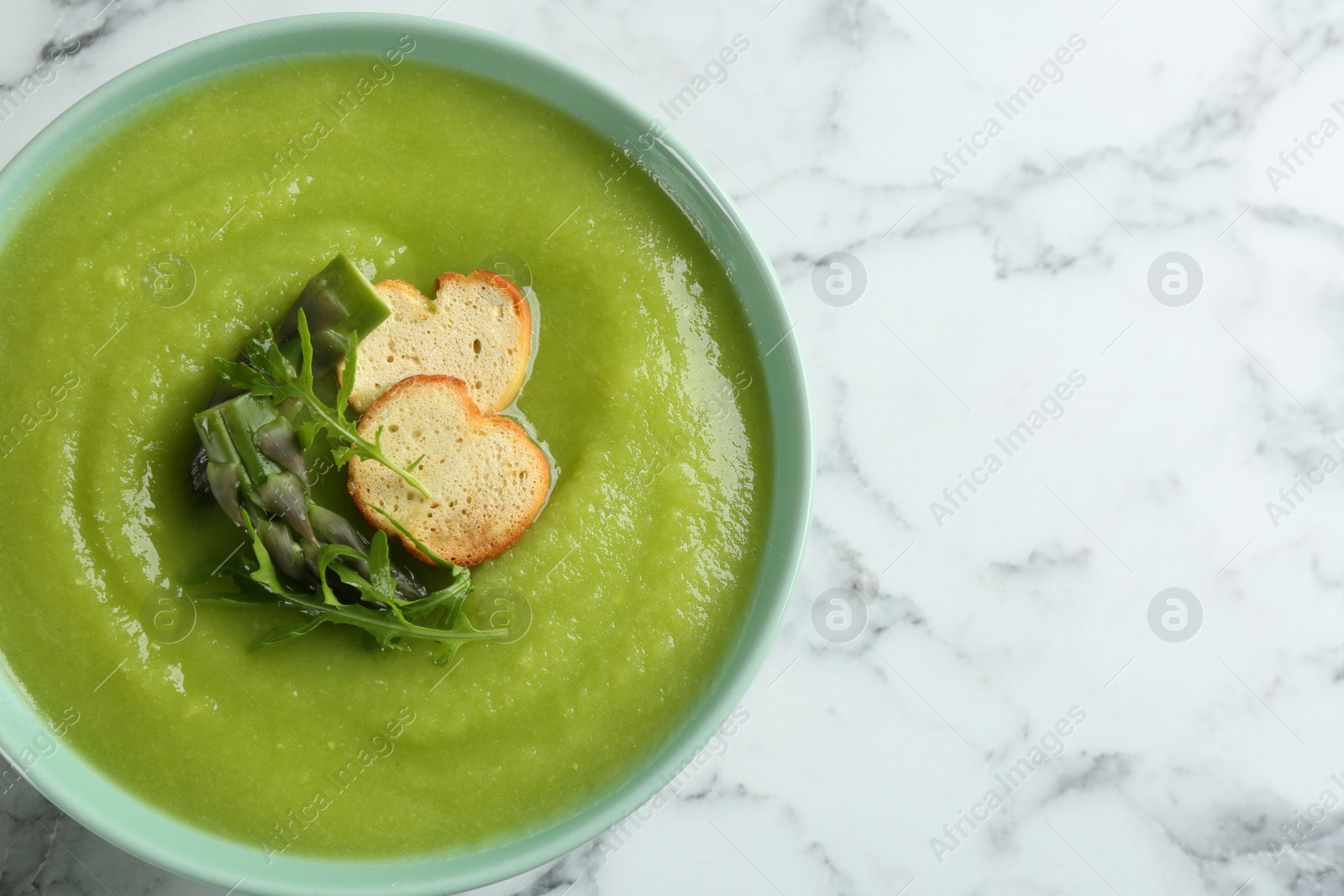 Photo of Delicious asparagus soup in bowl on white marble table, top view. Space for text