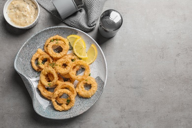 Photo of Homemade crunchy fried onion rings and sauce on gray background, top view. Space for text