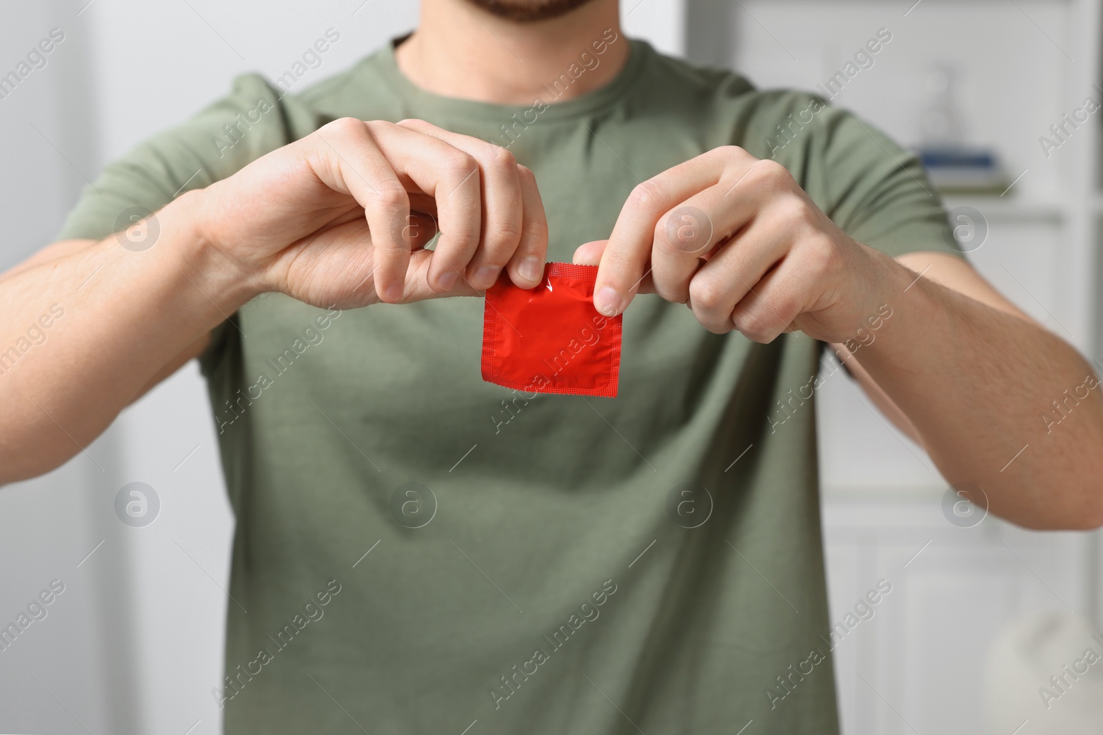 Photo of Closeup view of man opening pack with condom indoors