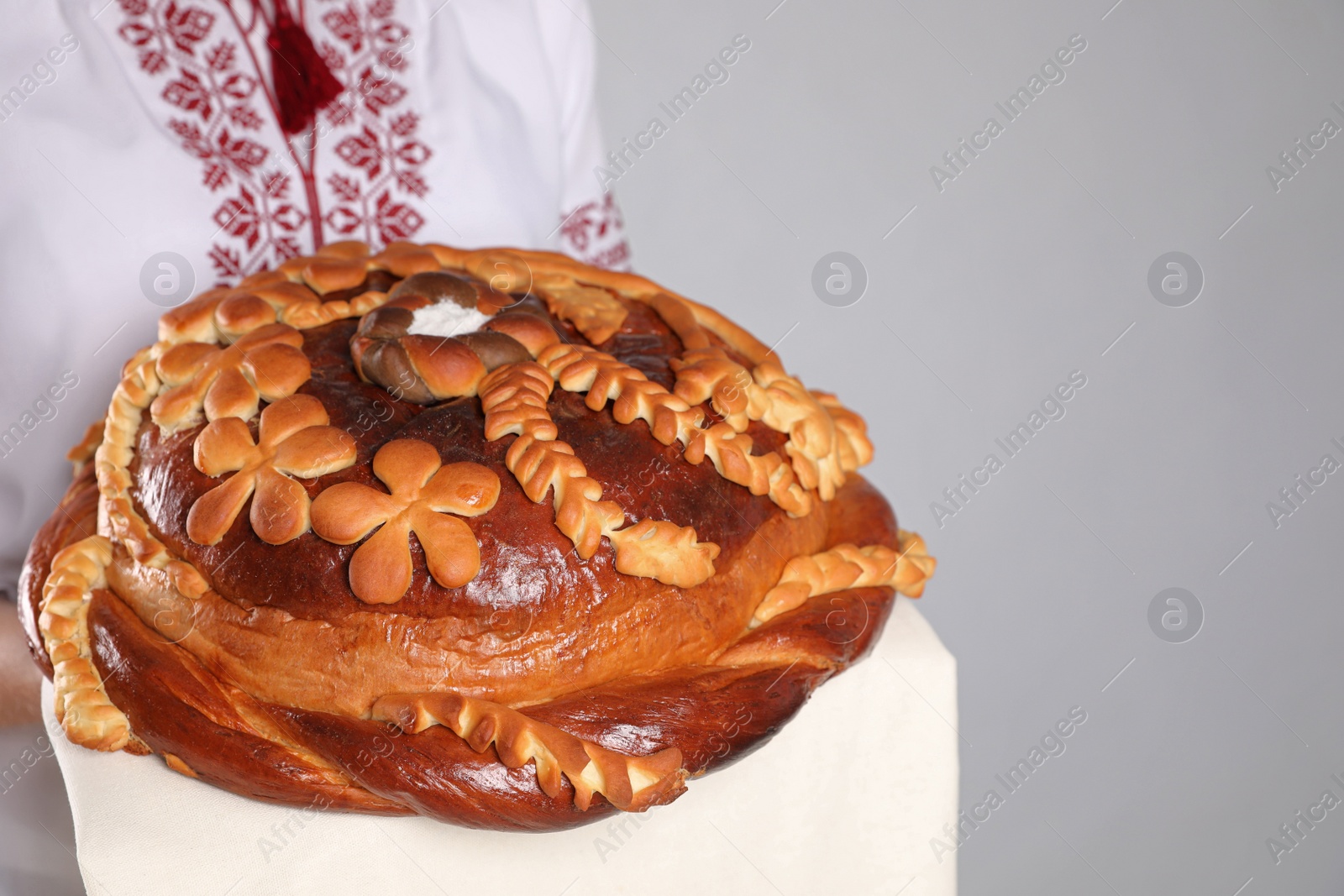 Photo of Woman holding korovai on grey background, closeup with space for text. Ukrainian bread and salt welcoming tradition