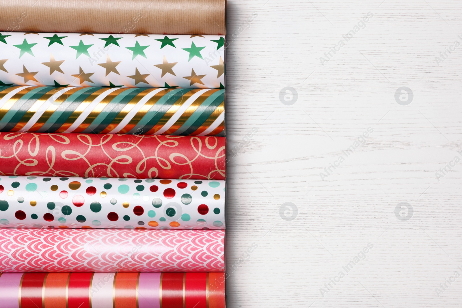 Photo of Different colorful wrapping paper rolls on white wooden table, flat lay. Space for text