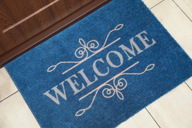 Photo of Beautiful blue doormat with word Welcome on floor near entrance, above view