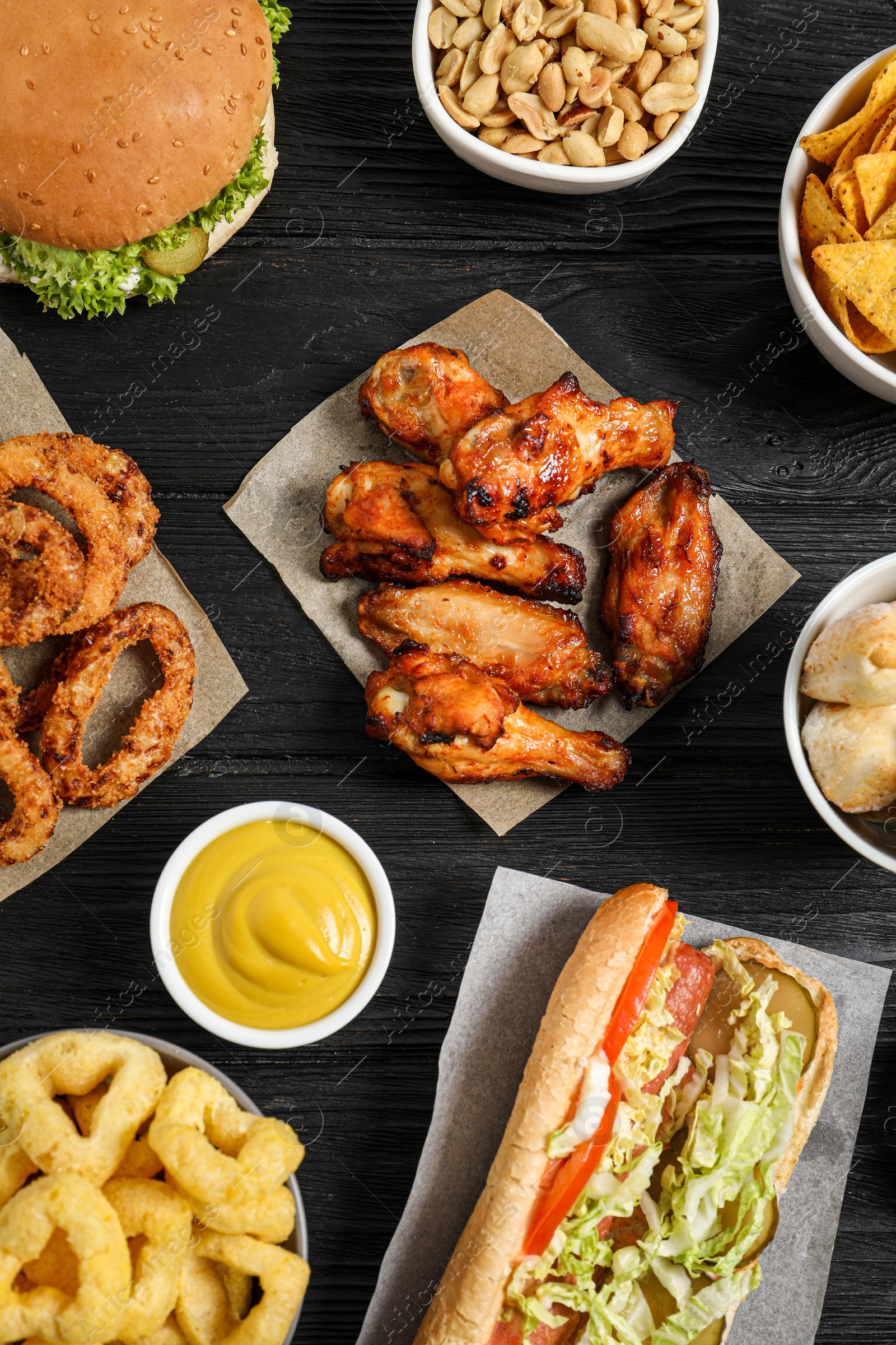 Photo of Chicken wings, onion rings and other fast food on black wooden table, flat lay