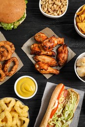 Chicken wings, onion rings and other fast food on black wooden table, flat lay