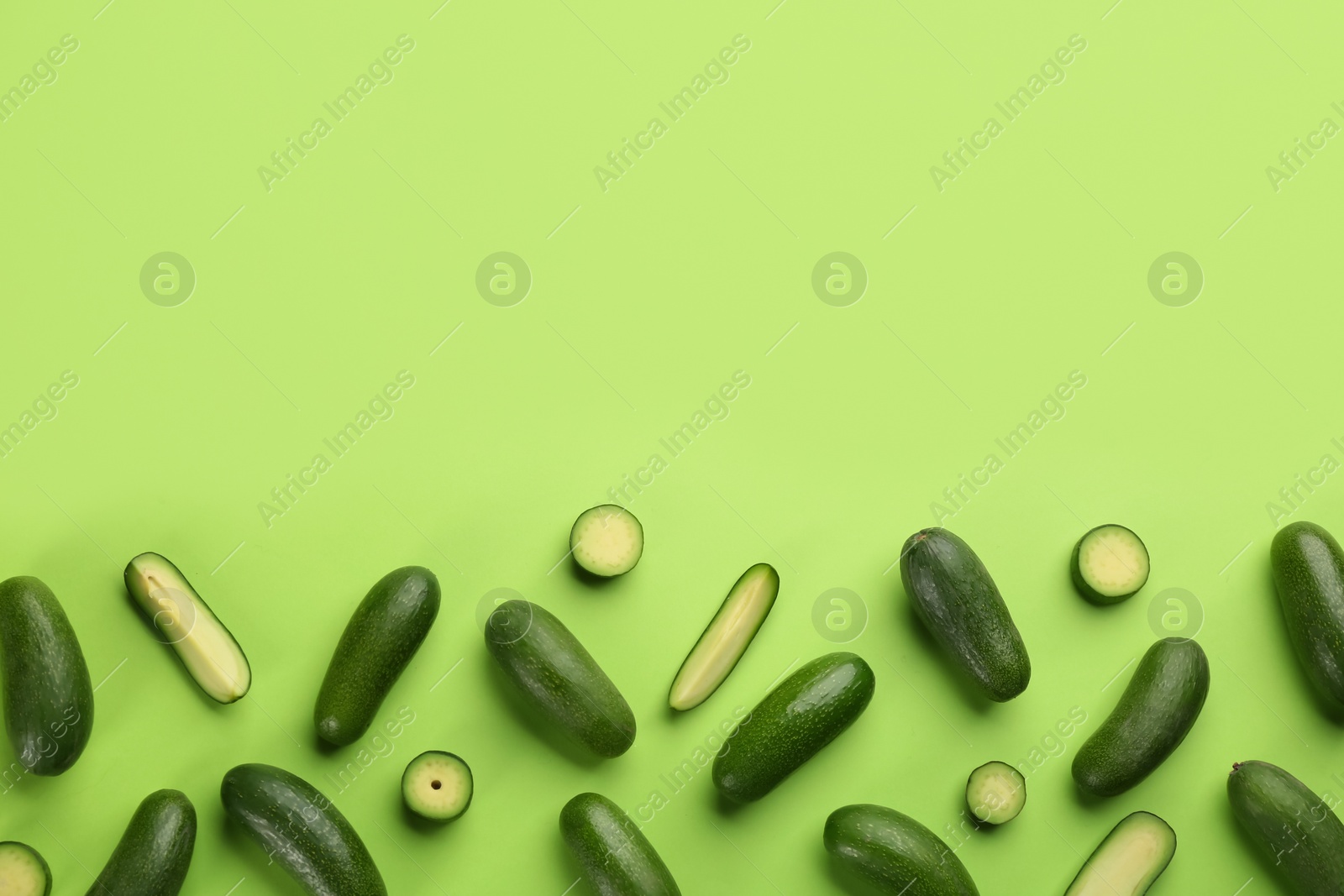 Photo of Whole and cut seedless avocados on green background, flat lay. Space for text