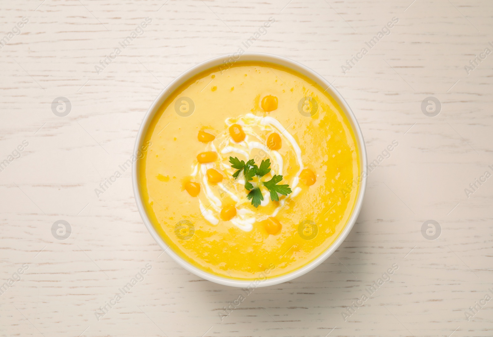 Photo of Delicious creamy corn soup served on white wooden table, top view