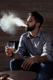 Man with glass of whiskey and cigar sitting at table indoors