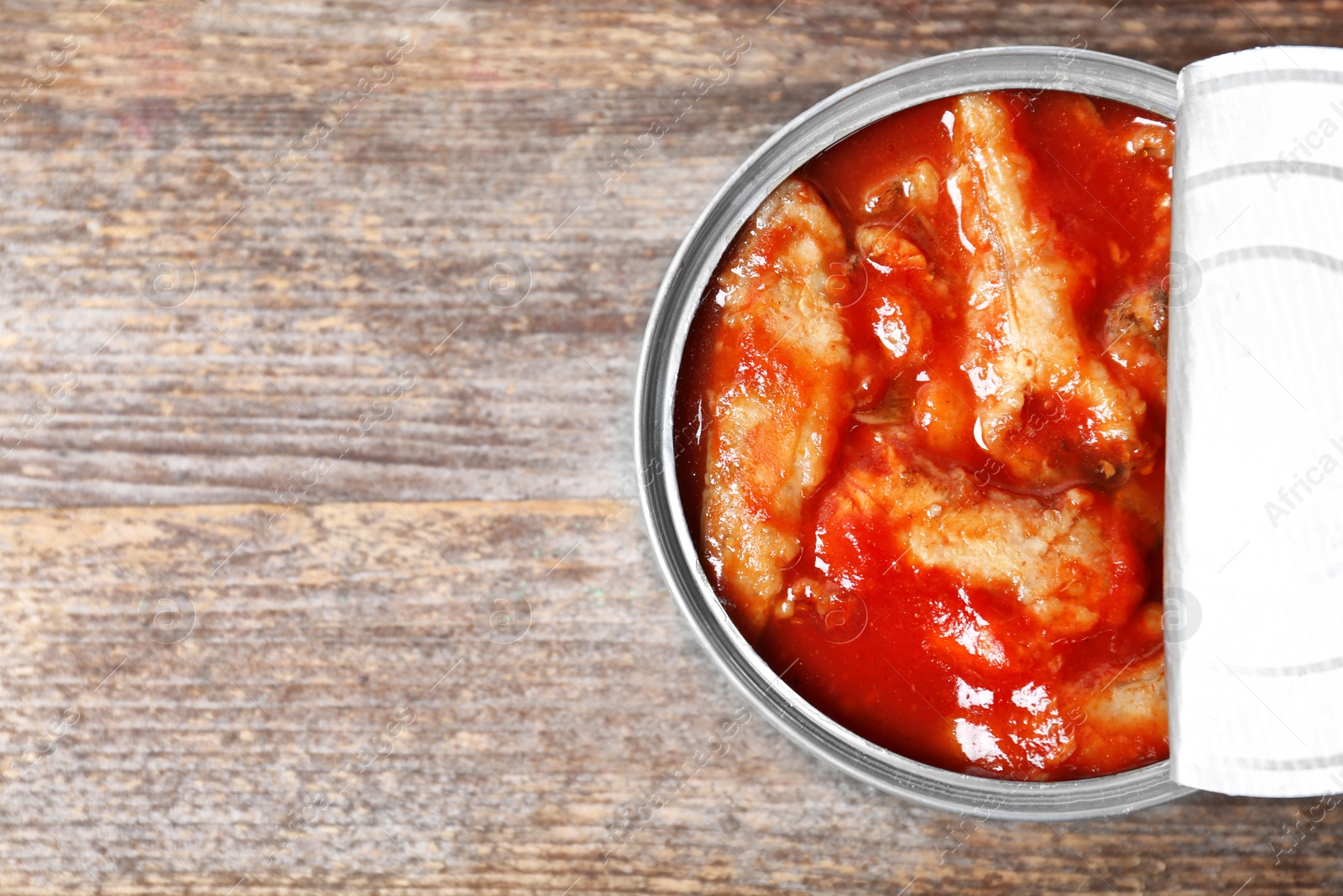 Photo of Tin can with conserved fish on wooden background, top view