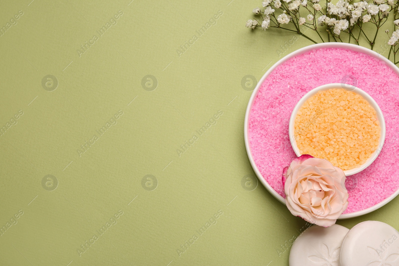 Photo of Sea salt, soap bars and beautiful flowers on olive background, flat lay. Space for text