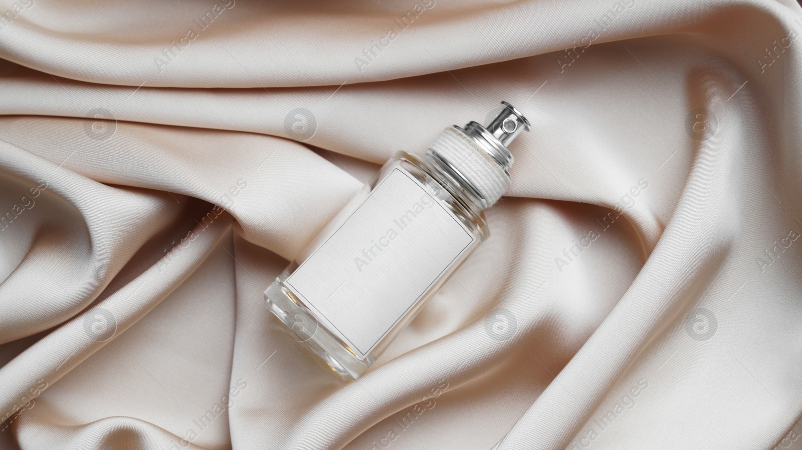 Photo of Luxury bottle of perfume on beige silk, top view