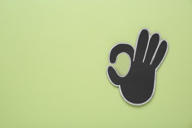 Paper cutout of okay hand gesture on pale olive background, top view. Space for text