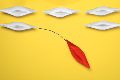 Photo of Red paper boat floating away from others on yellow background, flat lay. Uniqueness concept