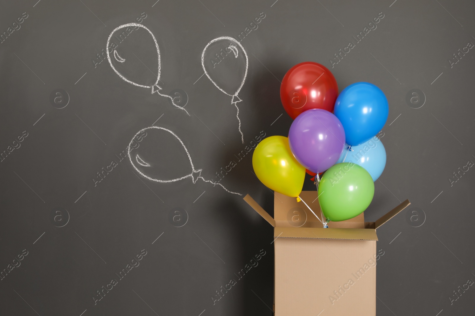 Photo of Gift box with bright air balloons and chalk drawing on grey background