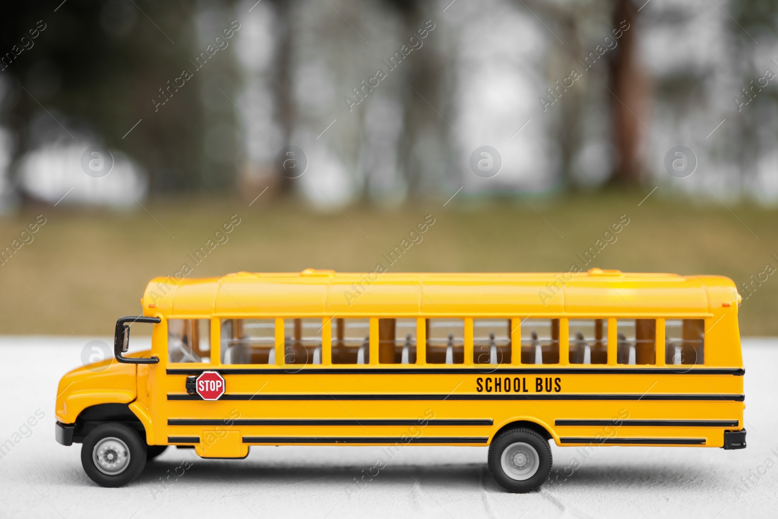 Photo of Yellow toy school bus against blurred background. Transport for students