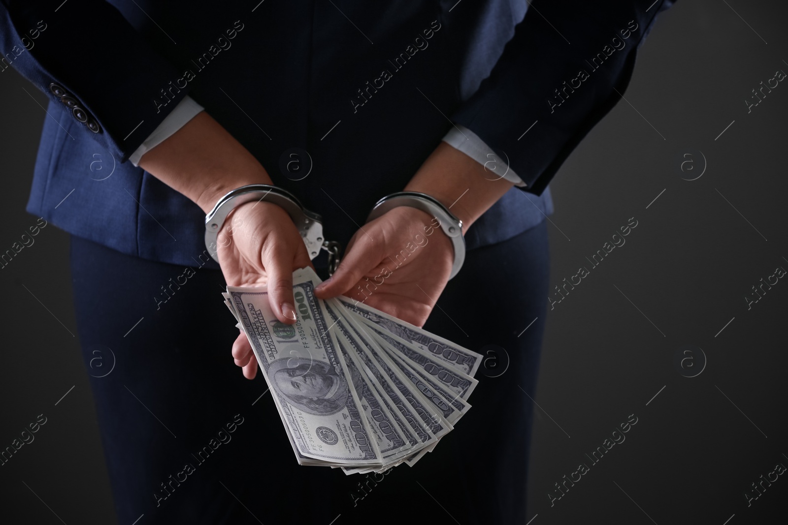 Photo of Woman in handcuffs holding bribe money on dark background, closeup