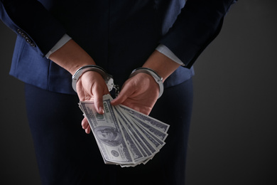 Woman in handcuffs holding bribe money on dark background, closeup