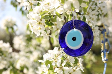Photo of Eye bead against evil eye hanging on blossoming tree outdoors, closeup