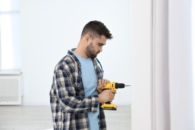 Photo of Young handyman working with electric drill at home