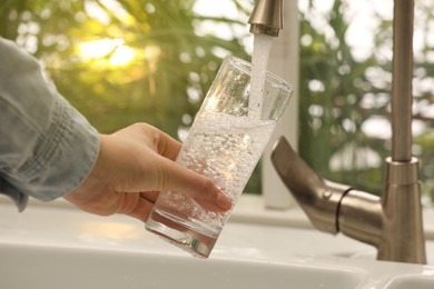 Woman filling glass with water from tap at home, closeup
