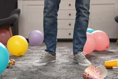 Photo of Man standing in messy room after party, closeup view of legs