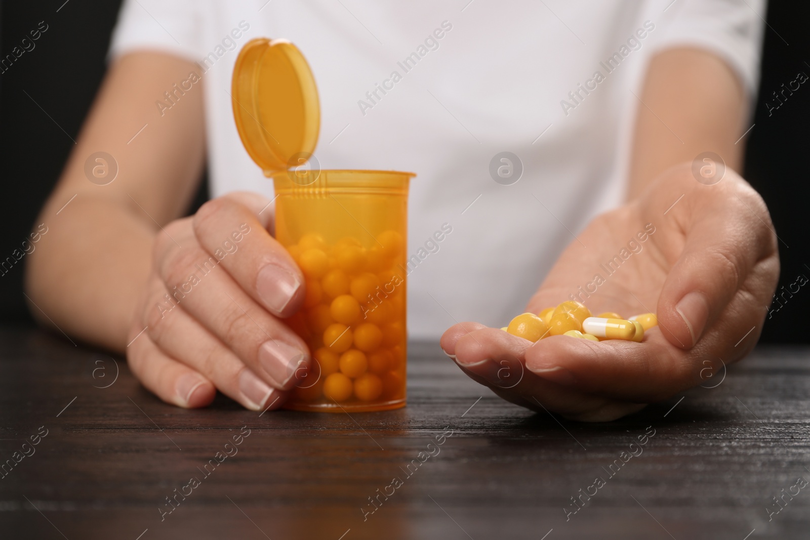 Photo of Woman holding different pills and bottle at table, closeup