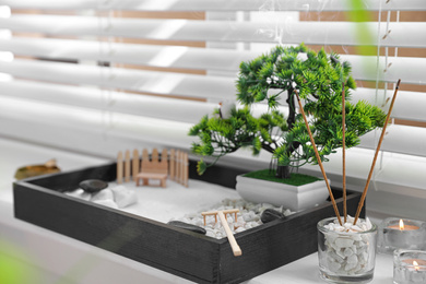 Photo of Beautiful miniature zen garden, candles and incense sticks on window sill
