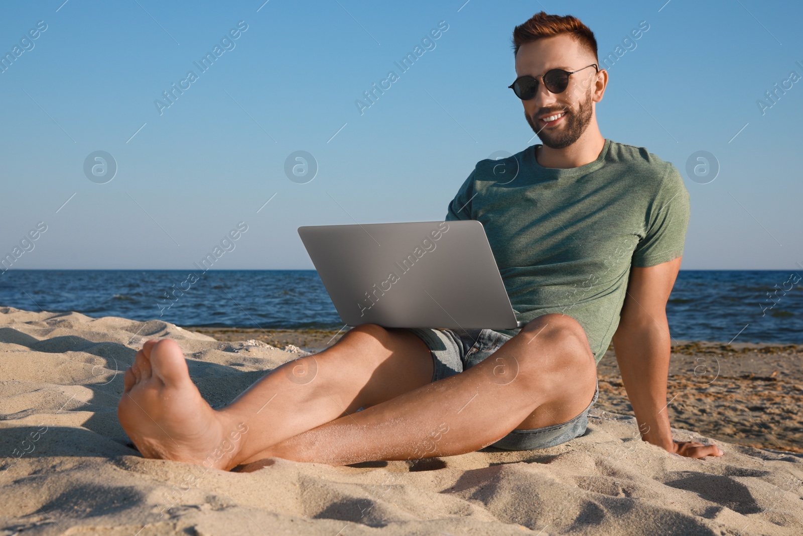 Photo of Man working with modern laptop on beach