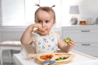 Photo of Cute little baby eating food in high chair at home