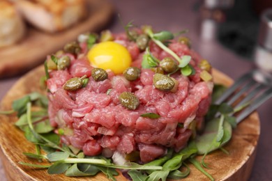 Photo of Tasty beef steak tartare served yolk, capers and microgreens on serving board, closeup