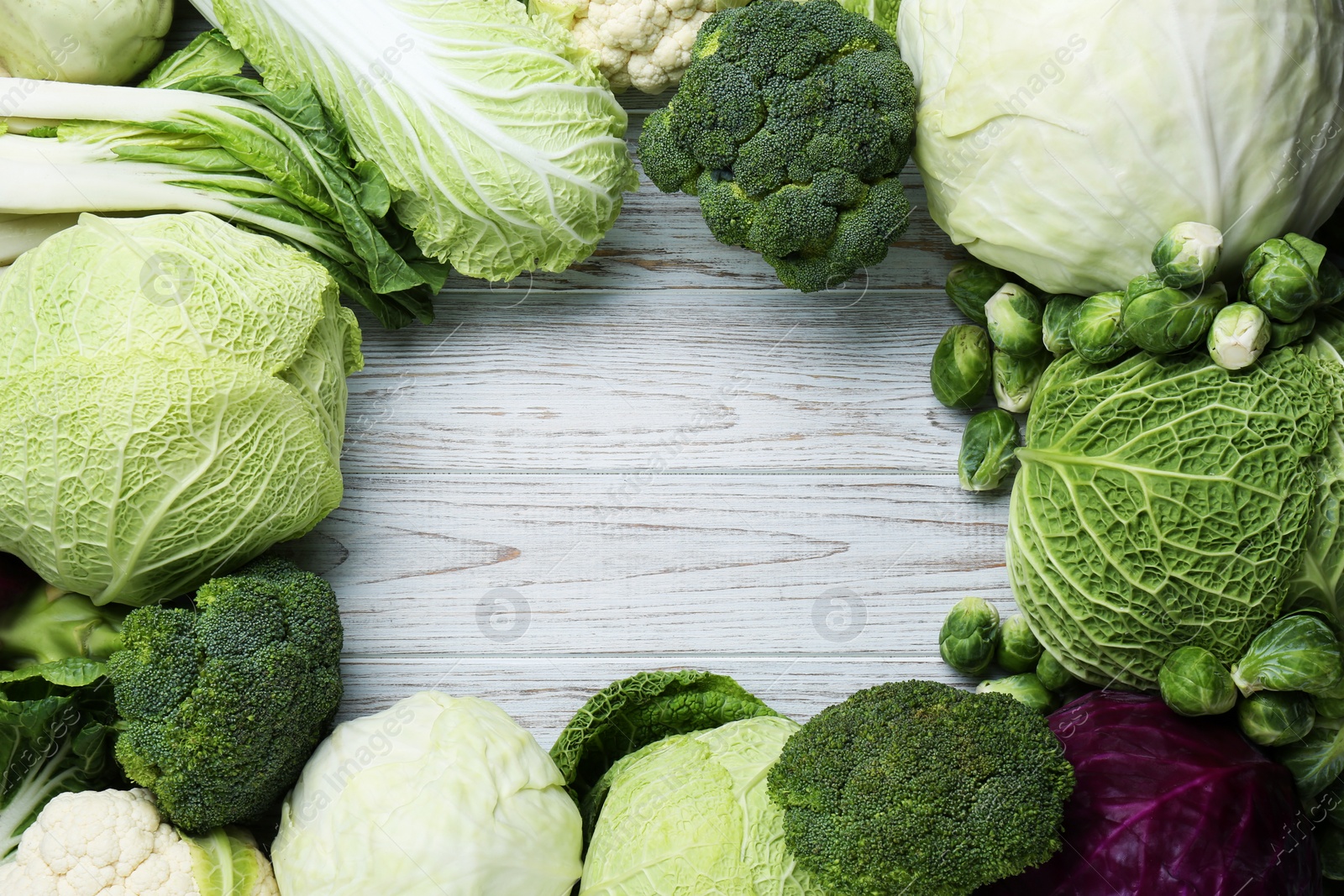 Photo of Frame of different cabbages on white wooden table, flat lay. Space for text