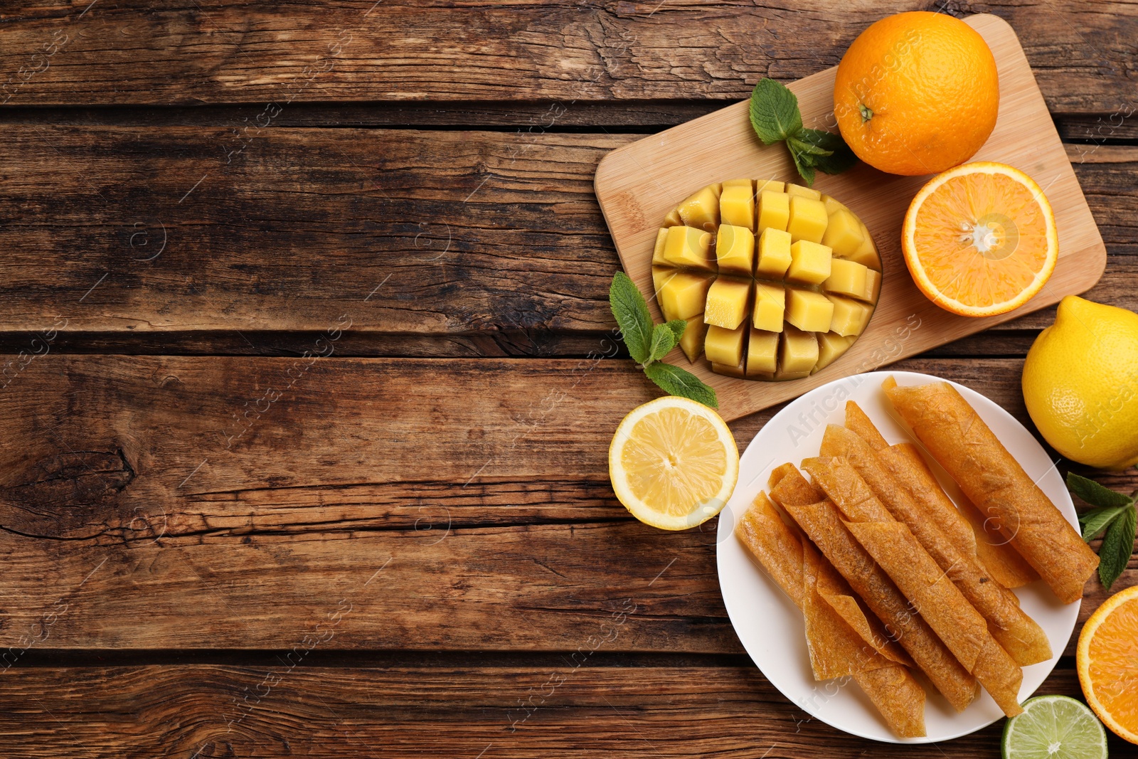 Photo of Flat lay composition with delicious fruit leather rolls on wooden table. Space for text