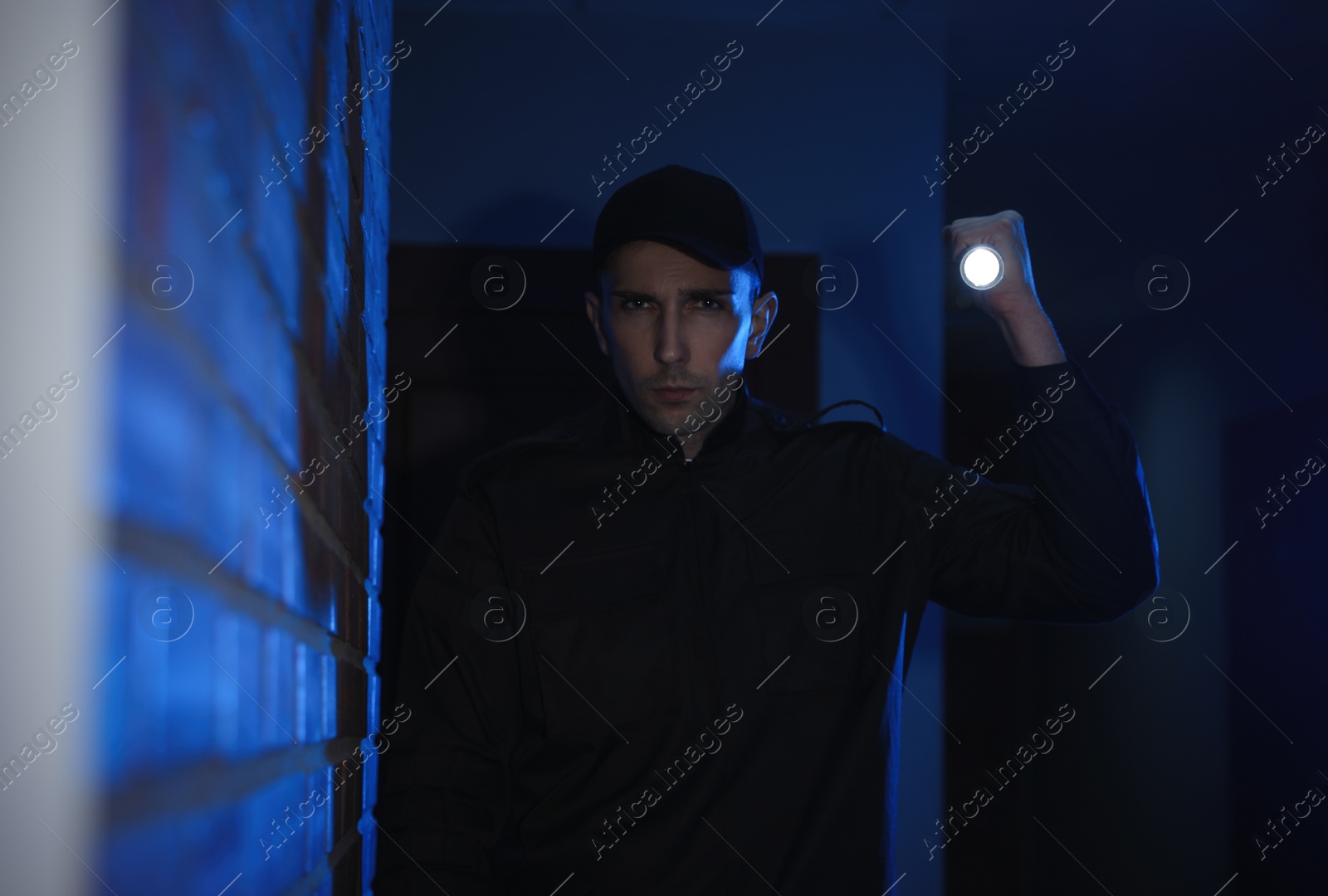 Photo of Male security guard with flashlight in dark corridor