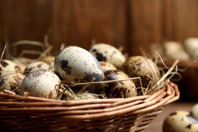 Photo of Wicker bowl with quail eggs and straw on blurred background, closeup