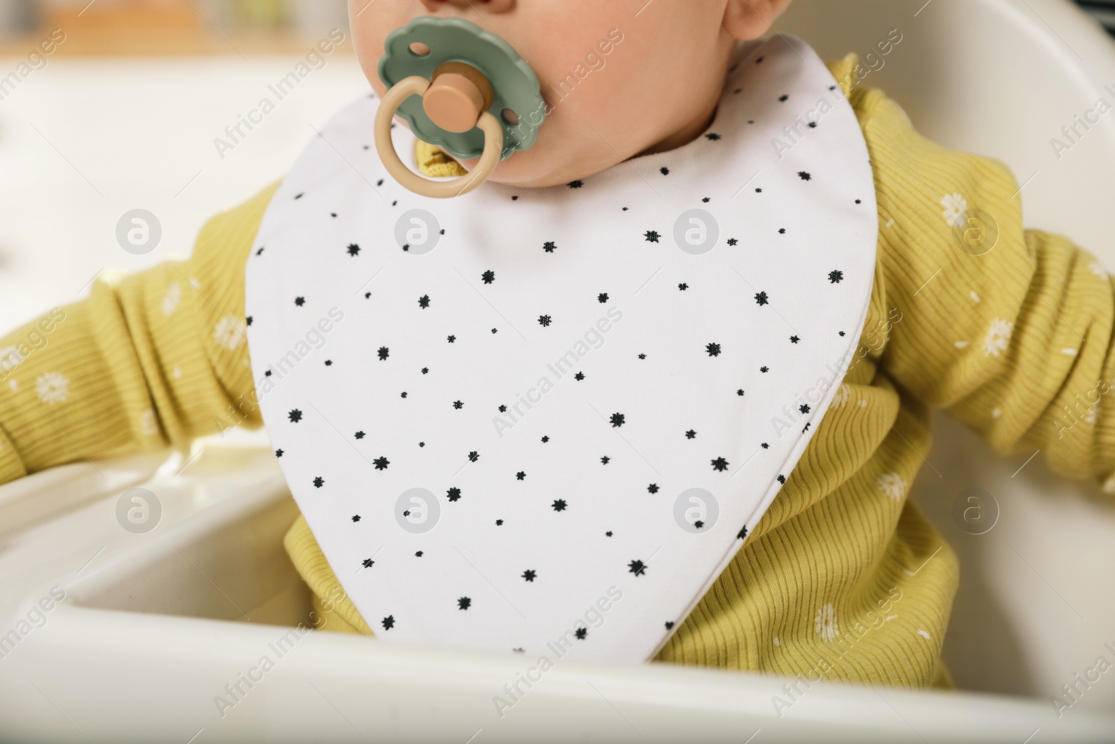 Photo of Cute little baby wearing bib in highchair, closeup